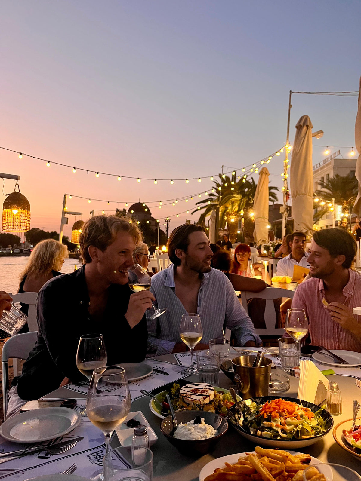 Drie vrienden aan tafel bij Poseidon op Poros, bij zonsondergang aan het water