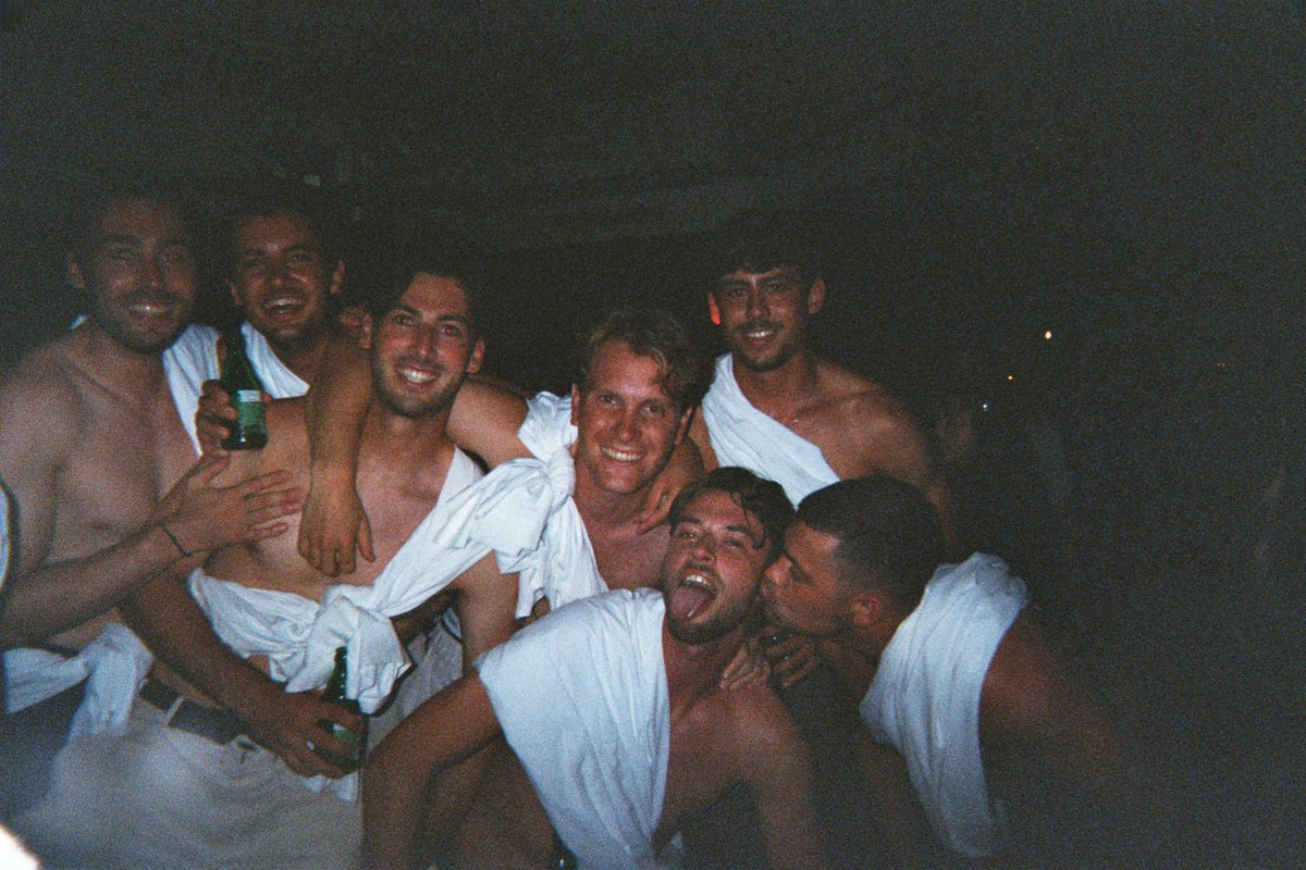 De crew als Griekse goden, met lakens als toga, bij Kastro Club op Agistri