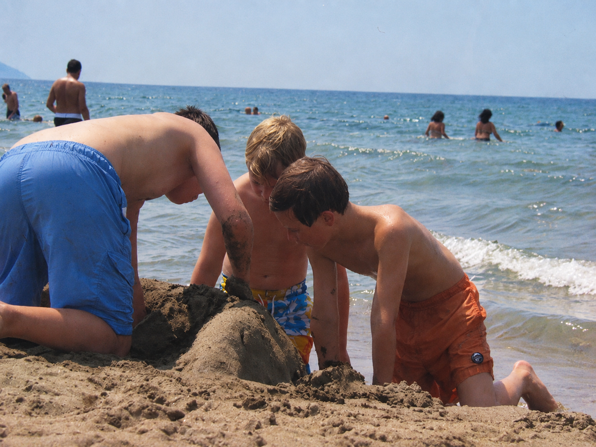 Drie jongens bouwen een zandkasteel aan de waterlijn tijdens de zomervakantie van 2009